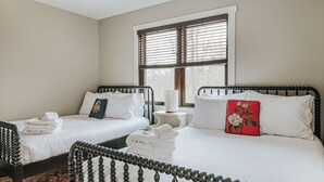 Una habitación de hotel con dos camas, una ventana con persianas, una mesita de noche y un cojín rojo.