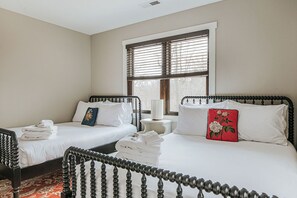 Una habitación de hotel con dos camas, una ventana con persianas, una mesita de noche y un cojín rojo.