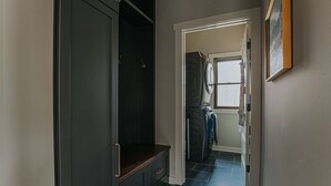 Un pasillo con un banco de madera oscura, zona de lavandería con lavadora y secadora, y una puerta que da a otra habitación.