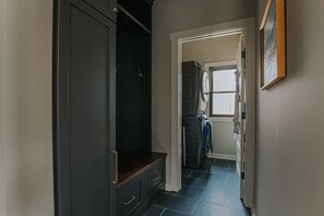 Un pasillo con un banco de madera oscura, zona de lavandería con lavadora y secadora, y una puerta que da a otra habitación.