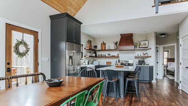 Una cocina moderna con armarios oscuros, una isla central y un comedor con mesa de madera y sillas verdes.