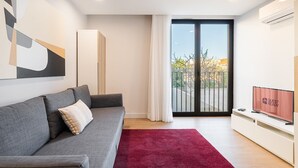 A modern living room with a grey sofa, a red rug, a TV on a stand, and a balcony with a glass door. - GuestReady - Soothing Comfort in Aveiro (Aveiro)