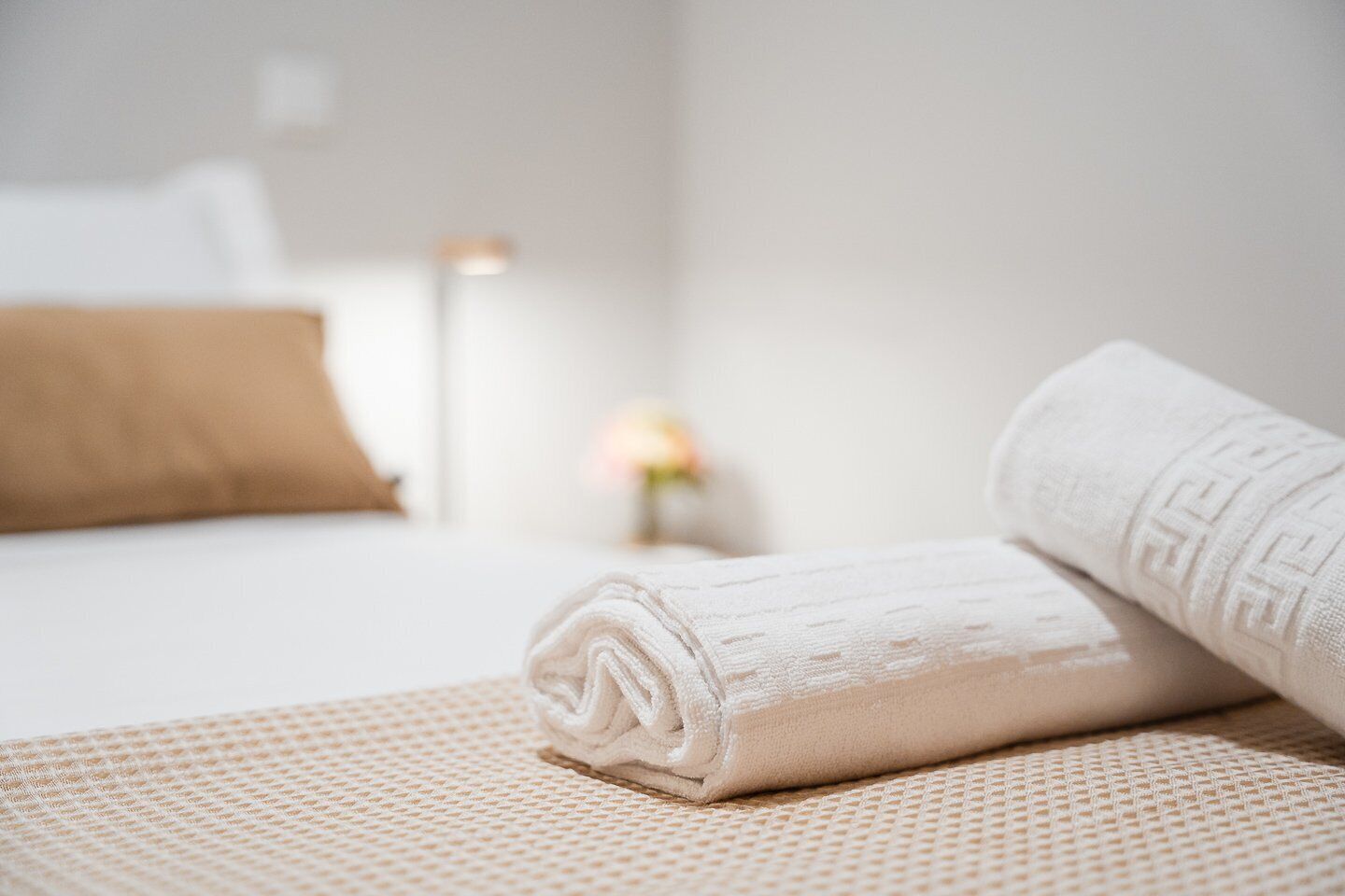 Una cama bien hecha con una toalla blanca enrollada y una almohada marrón.