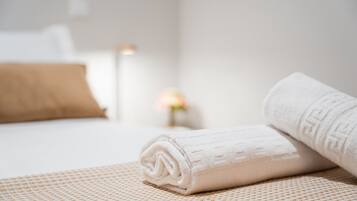 Una cama bien hecha con una toalla blanca enrollada y una almohada marrón.