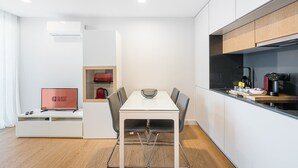 A modern kitchen with a dining area, white cabinetry, and a built-in coffee machine. - GuestReady - Soothing Comfort in Aveiro (Aveiro)