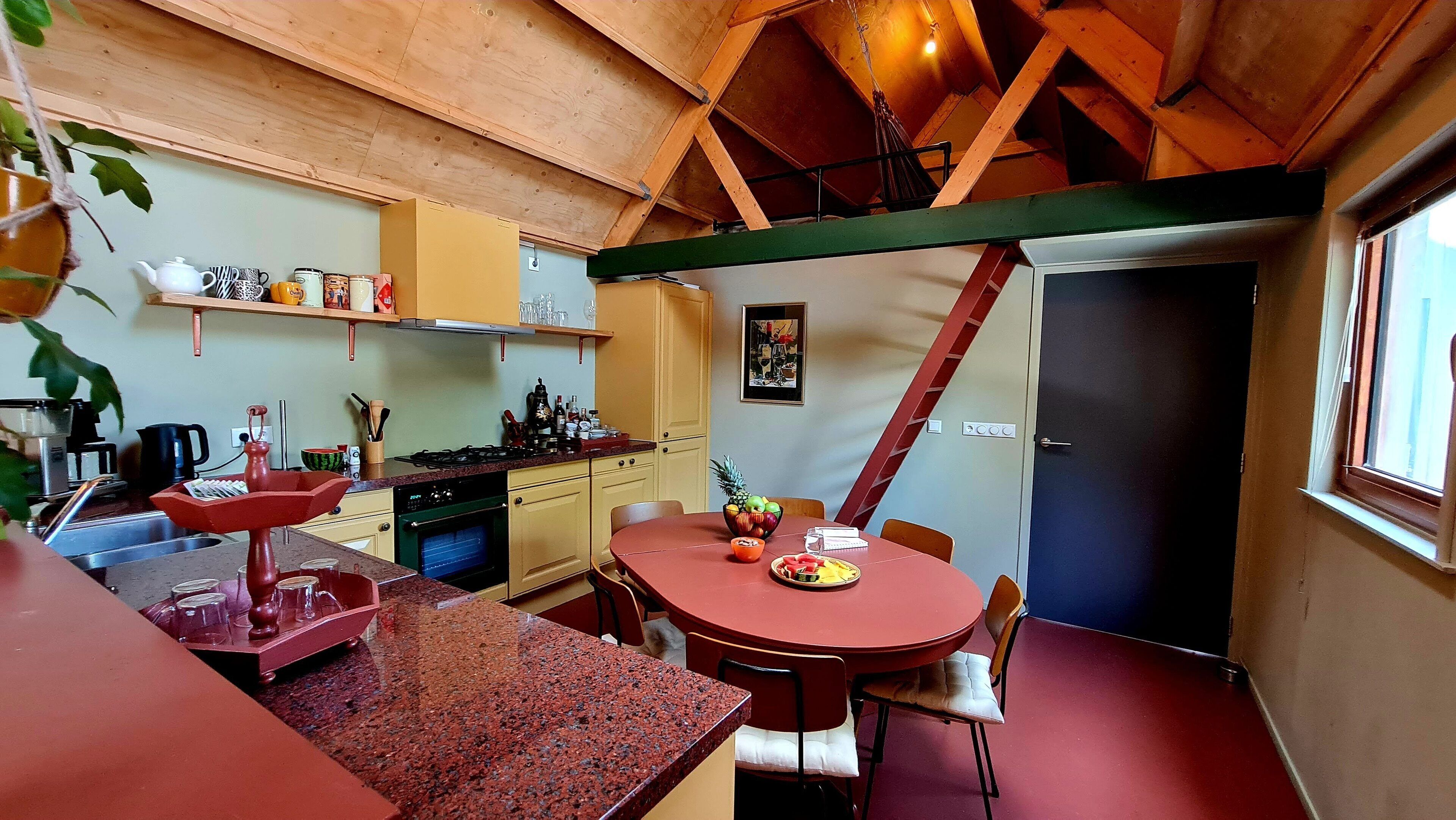 A compact kitchen with a dining area, featuring a red table, a stove, and a sink.