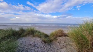 Une plage avec des dunes de sable et de l’herbe au premier plan, qui s’étend jusqu’à l’océan.