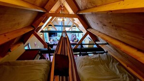 Une pièce en bois aux hauts plafonds et au toit en pente, avec un hamac et une vue sur l’extérieur.