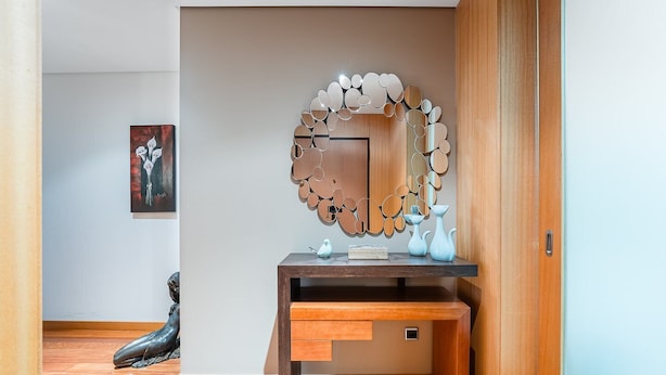 Une salle de bain moderne avec un meuble-lavabo en bois, un miroir décoratif et une petite sculpture posée sur le sol.