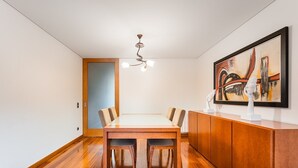 Un espace repas moderne avec une table et des chaises en bois, un luminaire au plafond et un tableau accroché au mur.