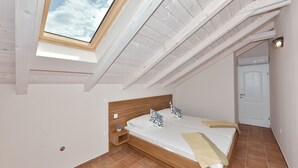 A bedroom with a skylight, wooden beams, a bed with pillows, a bedside table, and a door. - Villa Lapis Zadar Villas (Donje Raštane)