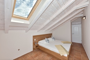 A bedroom with a skylight, wooden beams, a bed with pillows, a bedside table, and a door. - Villa Lapis Zadar Villas (Donje Raštane)