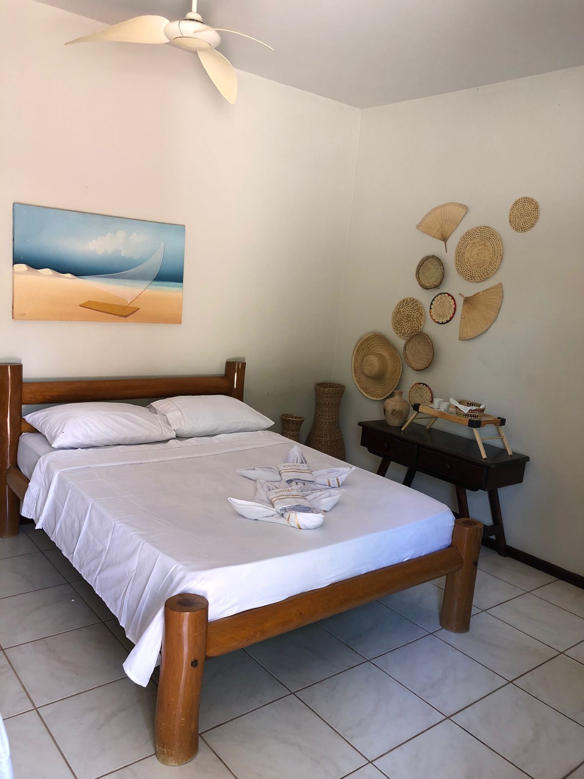 Una cama bien hecha con sábanas blancas, cabecera de madera y un ventilador de techo.