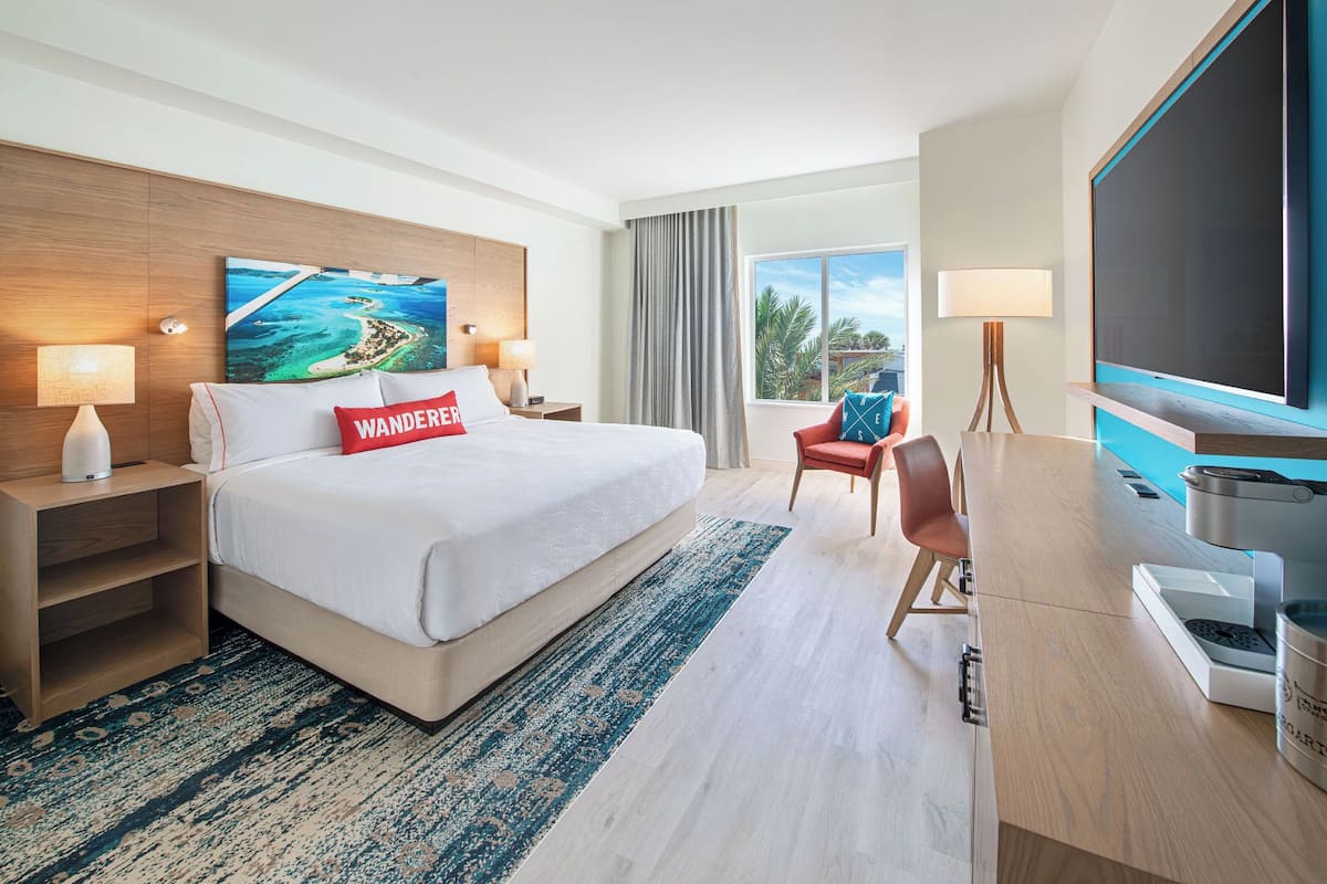 A hotel room with a large bed, a desk, a TV, and a painting on the wall.