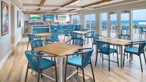 A spacious bar area with a view of the ocean, featuring wooden beams, blue chairs, and a bar counter with various bottles. - Compass Hotel Flagler Beach (Flagler Beach)