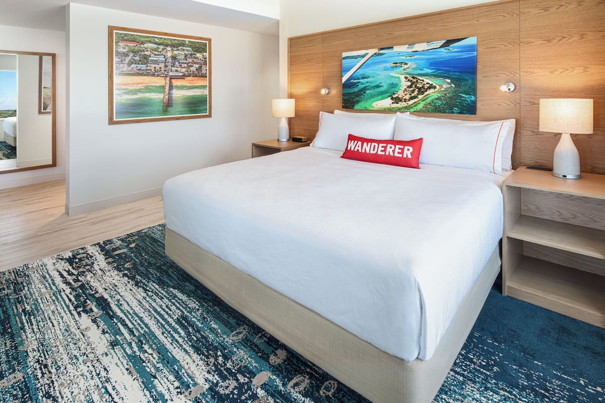 A hotel room with a large bed, two bedside tables with lamps, a wooden headboard, and two paintings on the walls.