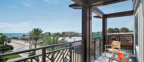 Un balcon avec vue sur la plage, une chaise en bois et une petite table.