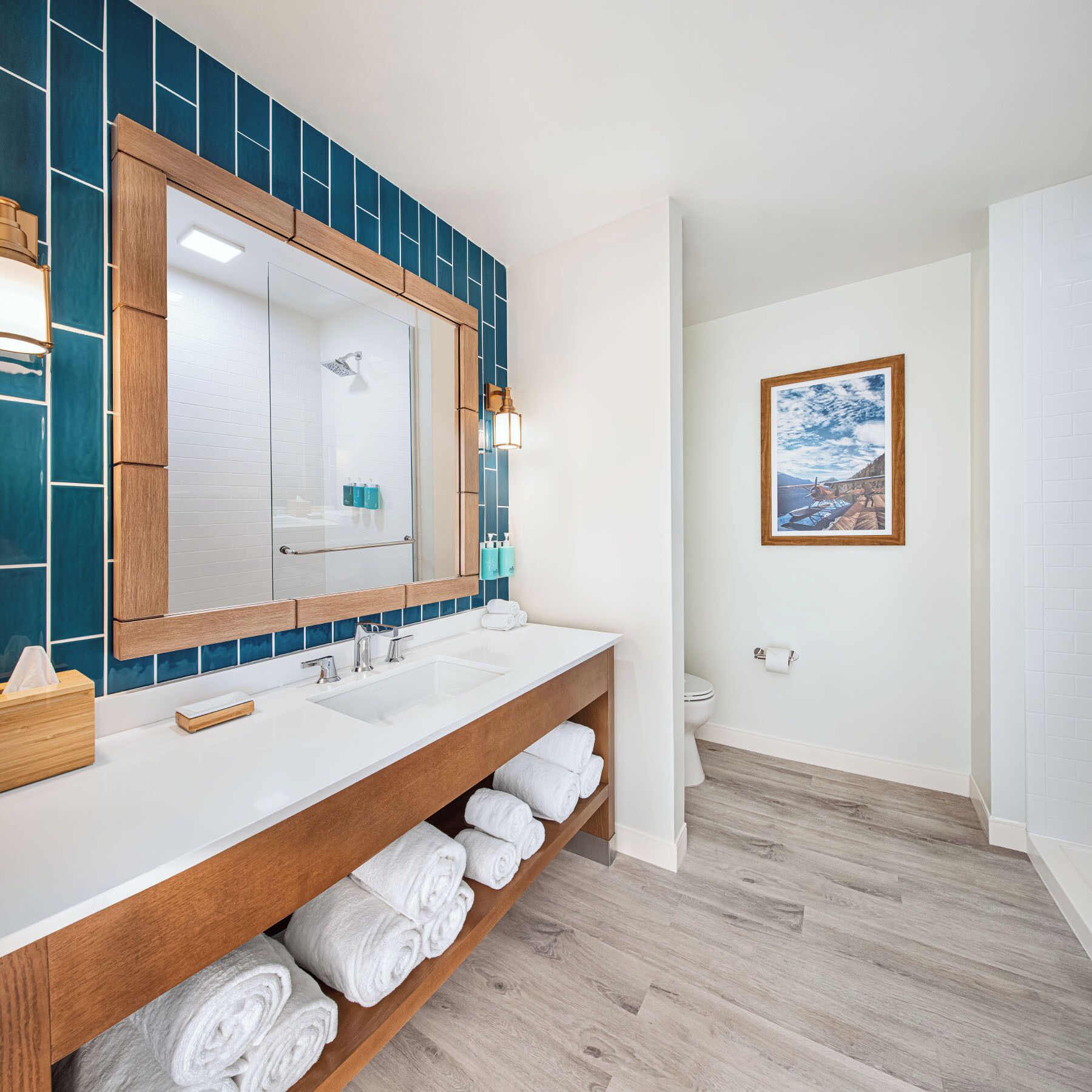 A modern bathroom with a large mirror, two sinks, and a wooden shelf with towels.