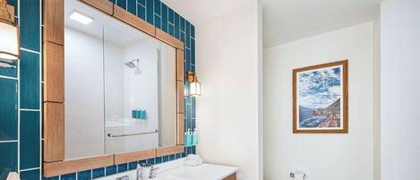 A modern bathroom with a large mirror, two sinks, and a wooden shelf with towels.