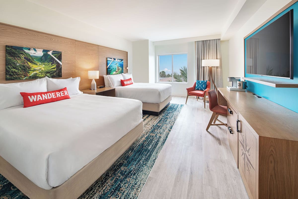 A hotel room with two beds, a desk, a chair, and a large window.