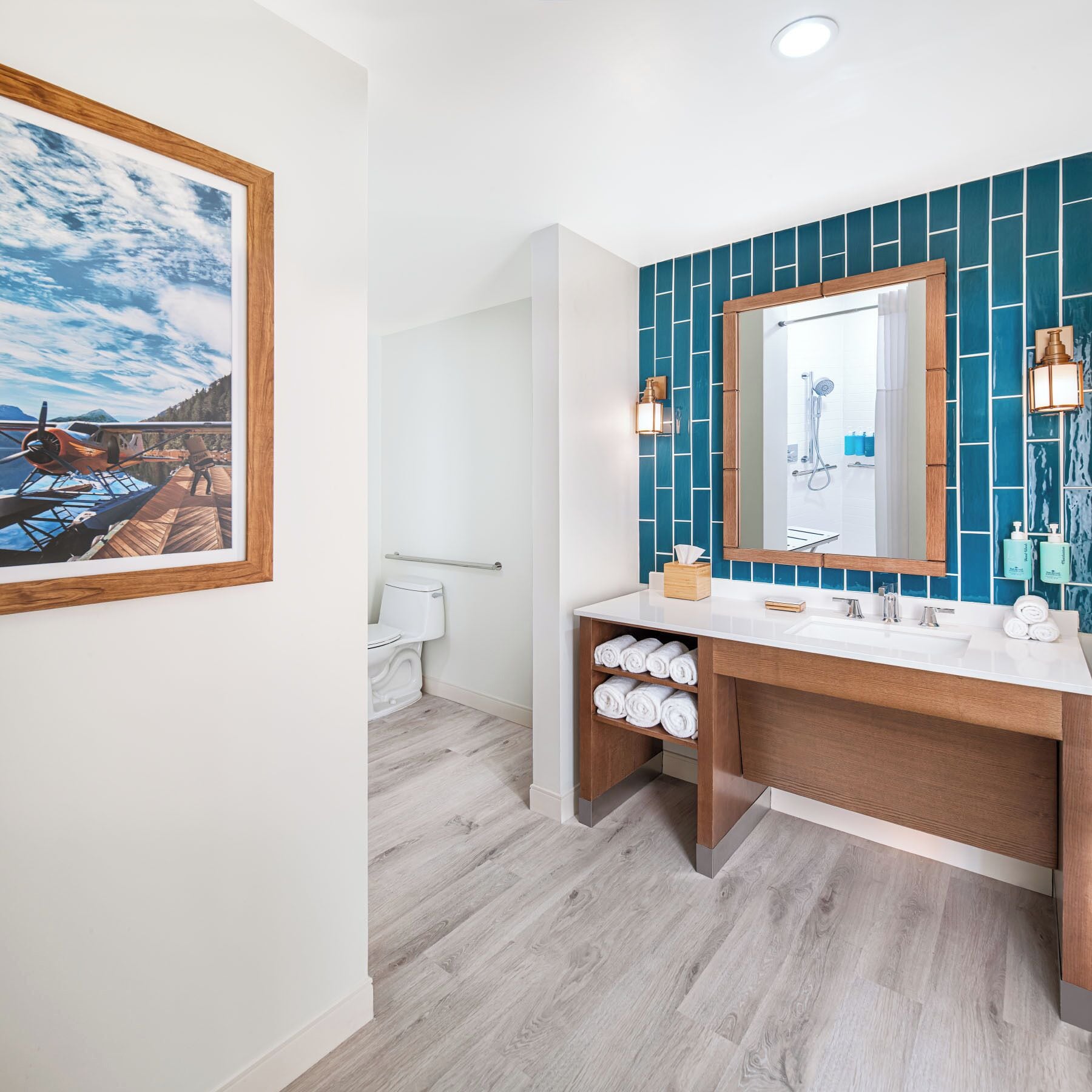 Un baño moderno con un lavamanos blanco, tocador de madera y pared de ducha con azulejos azules.