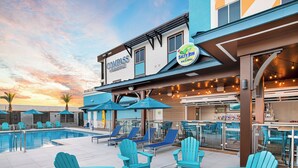 A poolside area with blue Adirondack chairs, a fire pit, and a bar area with a sign for 'Salty Rim Bar & Grill'. - Compass Hotel Flagler Beach (Flagler Beach)