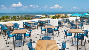 An outdoor seating area with tables and chairs, overlooking a beach and ocean. - Compass Hotel Flagler Beach (Flagler Beach)