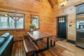 A wooden cabin interior with a dining table, benches, a sofa, a door, and a refrigerator. - Frog Hill | Hocking Hills, EV Charger, Hot Tub (Logan)