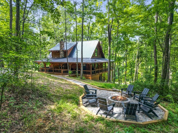 A cabin with a stone chimney, wooden deck, and a fire pit surrounded by Adirondack chairs. - Frog Hill | Hocking Hills, EV Charger, Hot Tub (Logan)