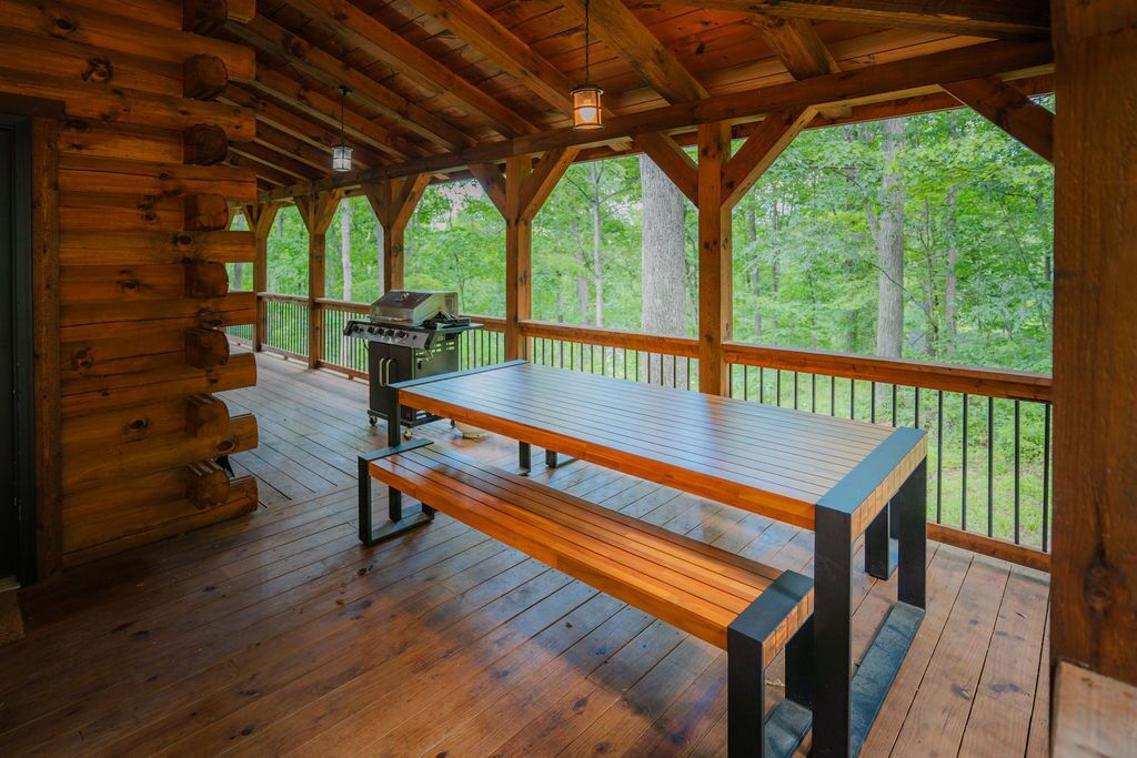 A wooden deck with a picnic table and grill, surrounded by a railing with a view of a forest.