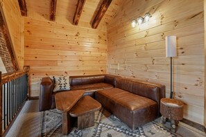 A cozy wooden cabin interior with a brown leather sofa, a small wooden table, and a lamp. - Frog Hill | Hocking Hills, EV Charger, Hot Tub (Logan)