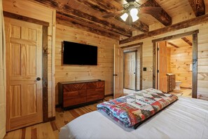 A wooden cabin bedroom with a bed, dresser, TV, and a ceiling fan.