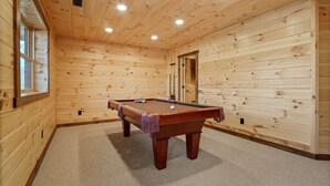 A wooden-paneled room with a pool table, carpeted floor, and a door leading to another room. - Frog Hill | Hocking Hills, EV Charger, Hot Tub (Logan)