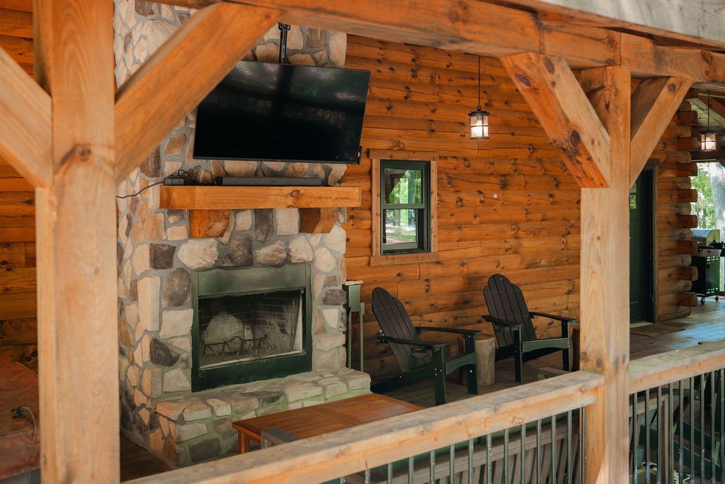 Ein Holzblockhaus-Interieur mit Kamin aus Stein, einem angebrachten Fernseher und zwei Adirondack-Stühlen.