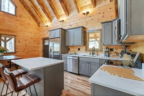 A modern kitchen with wooden walls, stainless steel appliances, and bar stools. - Frog Hill | Hocking Hills, EV Charger, Hot Tub (Logan)