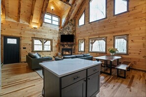 A spacious cabin interior with a stone fireplace, wooden walls, a large dining table, and a cozy seating area. - Frog Hill | Hocking Hills, EV Charger, Hot Tub (Logan)