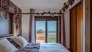 A bedroom with a bed, a wooden headboard, a view of the sea, and a balcony.
