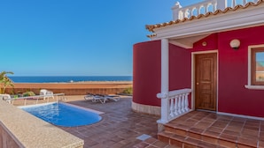 A red building with a pool and a view of the sea.