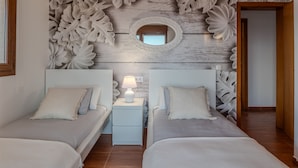 A bedroom with two beds, a nightstand with a lamp, and a decorative wall with leaf patterns.