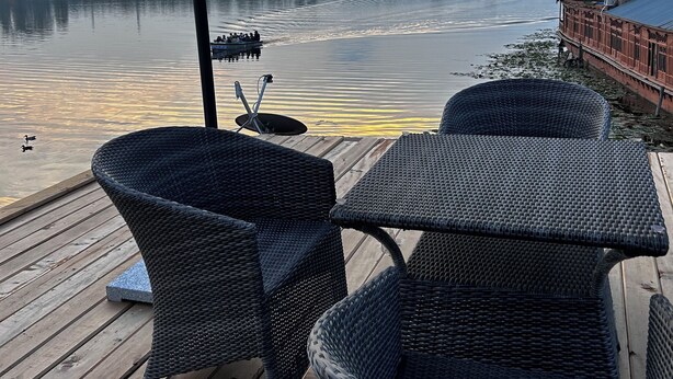 Terraza de madera con muebles de mimbre y vista a un río con un bote.