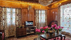 Una habitación tradicional con paneles de madera decorados, una araña, un televisor y adornos florales.
