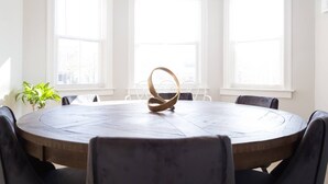Una mesa redonda con un centro de mesa original, rodeada de sillas, en una habitación con ventanas amplias y una planta en maceta.