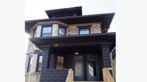Una casa moderna de dos pisos con fachada oscura, una puerta principal y una escalera de madera que conduce a la entrada.
