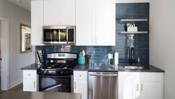 Una cocina moderna con armarios blancos, estufa de acero inoxidable, microondas y lavavajillas.