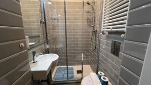 Un bany modern amb plat de dutxa envoltat per vidre, un lavabo i un vàter.
