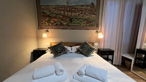 Habitació d'hotel amb un llit gran, dos almoines, dues làmpades de nit, un quadre d'una vista urbana i dues tovelloles arremolinades damunt el llit.
