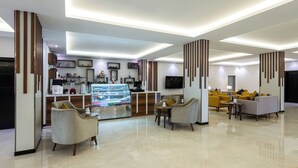 A modern hotel lobby with a central counter, seating area, and a large TV screen. - Al Qasr Hotel Suites -Al Masyaf District (Khamis Mushait)