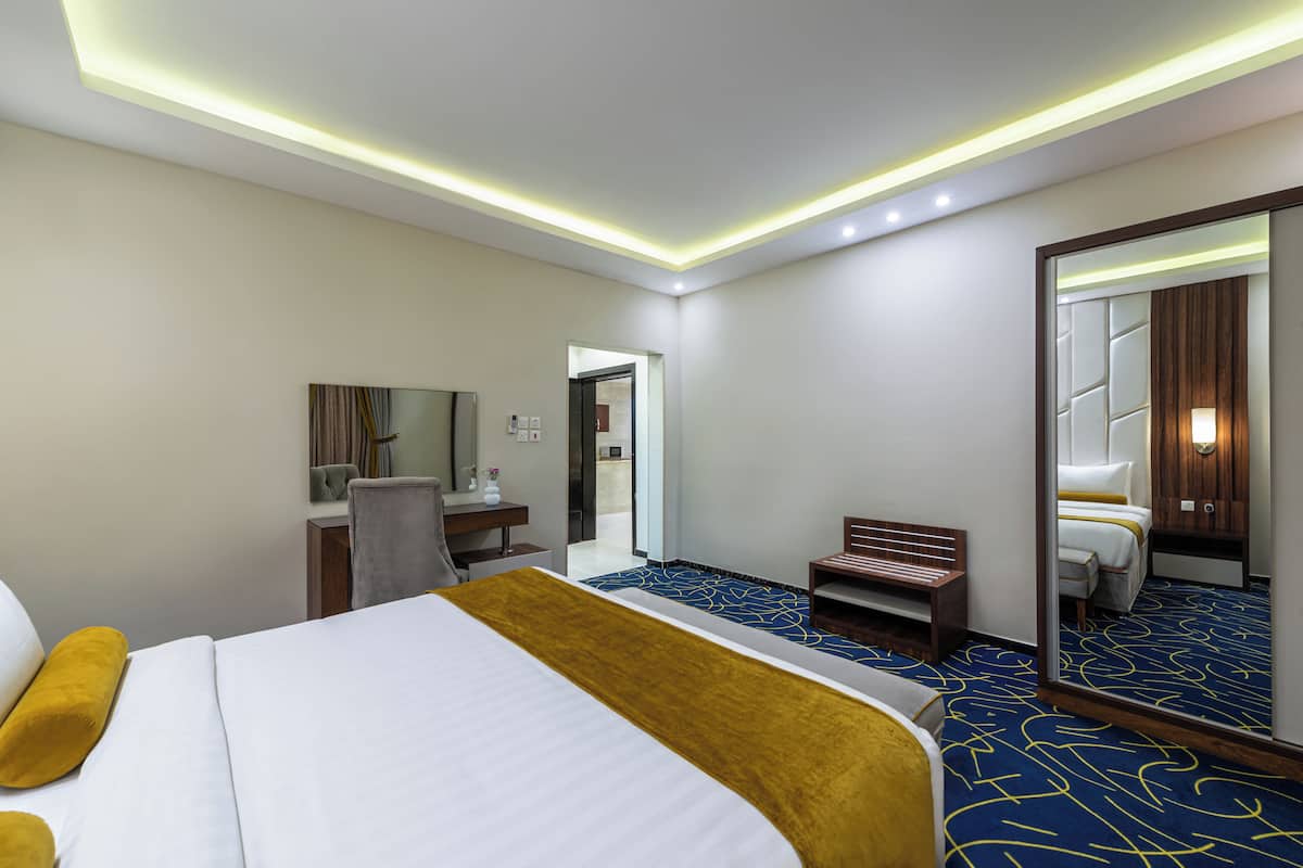 A hotel room with a bed, a desk, a chair, a mirror, and a bathroom visible through an open door.