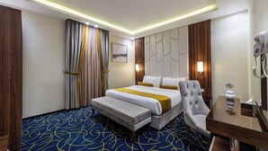 A hotel room with a large bed, a bedside table, a chair, and a desk. - Al Qasr Hotel Suites -Al Masyaf District (Khamis Mushait)