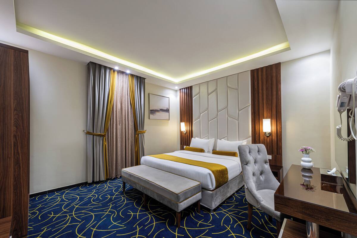 A hotel room with a large bed, a bedside table, a chair, and a desk.
